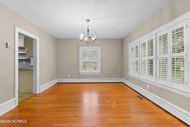 unfurnished dining area featuring baseboard heating, a chandelier, light hardwood / wood-style flooring, and a textured ceiling