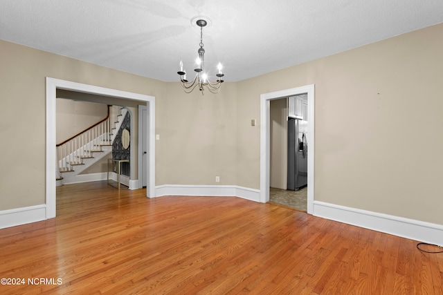 unfurnished room featuring hardwood / wood-style flooring, a notable chandelier, and a textured ceiling