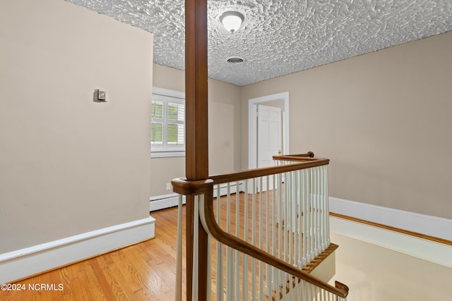 hall with hardwood / wood-style flooring, a baseboard radiator, and a textured ceiling