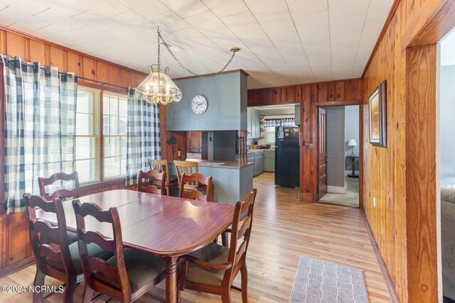 dining area featuring a notable chandelier, light hardwood / wood-style flooring, and wooden walls