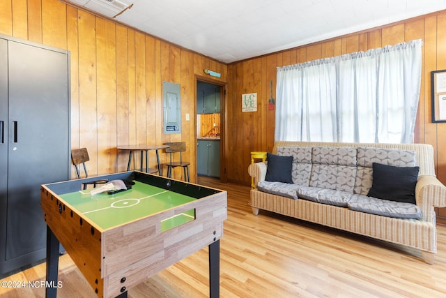 rec room featuring light wood-style floors, electric panel, and wood walls