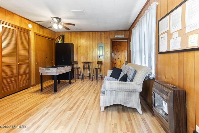 sitting room with light hardwood / wood-style floors, wooden walls, and ceiling fan