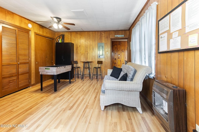 living area with light wood-style floors, wood walls, heating unit, and ceiling fan