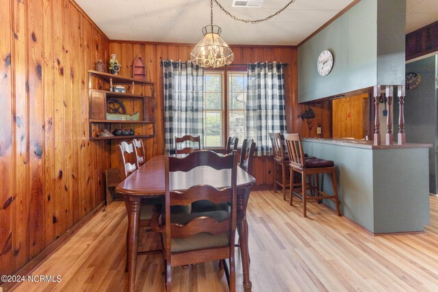 dining space featuring light wood-type flooring, wooden walls, and ornamental molding