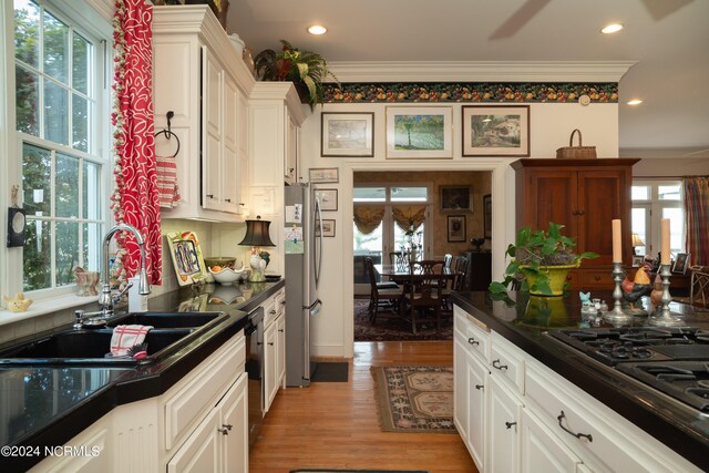 kitchen with appliances with stainless steel finishes, sink, crown molding, white cabinetry, and hardwood / wood-style flooring