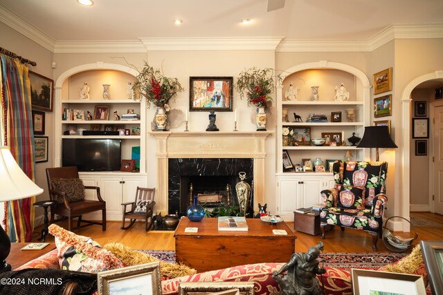 living room featuring a fireplace, wood-type flooring, built in shelves, and ornamental molding