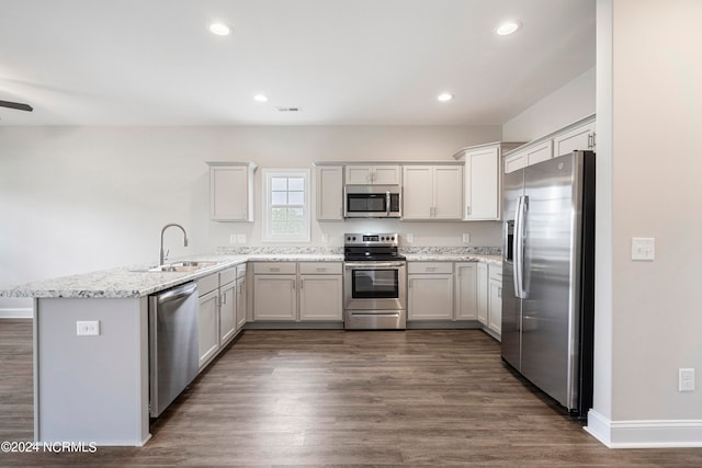 kitchen with stainless steel appliances, sink, kitchen peninsula, light stone counters, and dark wood-type flooring