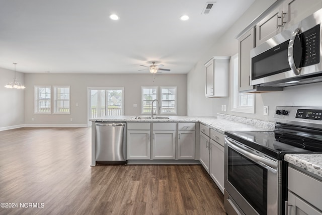 kitchen with appliances with stainless steel finishes, sink, kitchen peninsula, ceiling fan with notable chandelier, and dark wood-type flooring