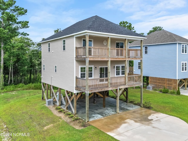 rear view of property with a carport, a balcony, a lawn, and central AC unit