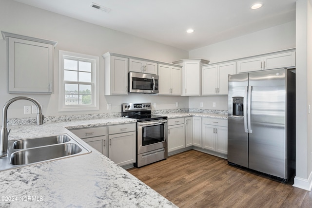 kitchen with sink, dark hardwood / wood-style floors, light stone counters, and stainless steel appliances