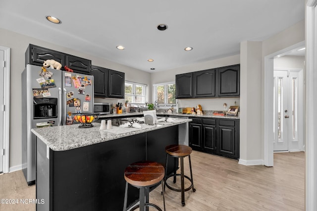 kitchen with light wood-type flooring, a kitchen breakfast bar, stainless steel appliances, light stone counters, and a kitchen island