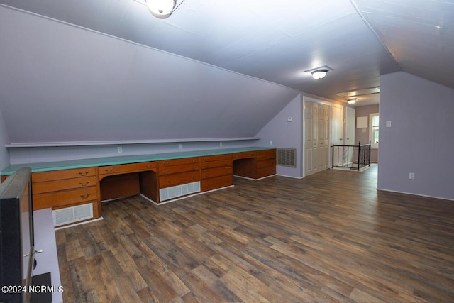 unfurnished office with vaulted ceiling, built in desk, and dark hardwood / wood-style flooring