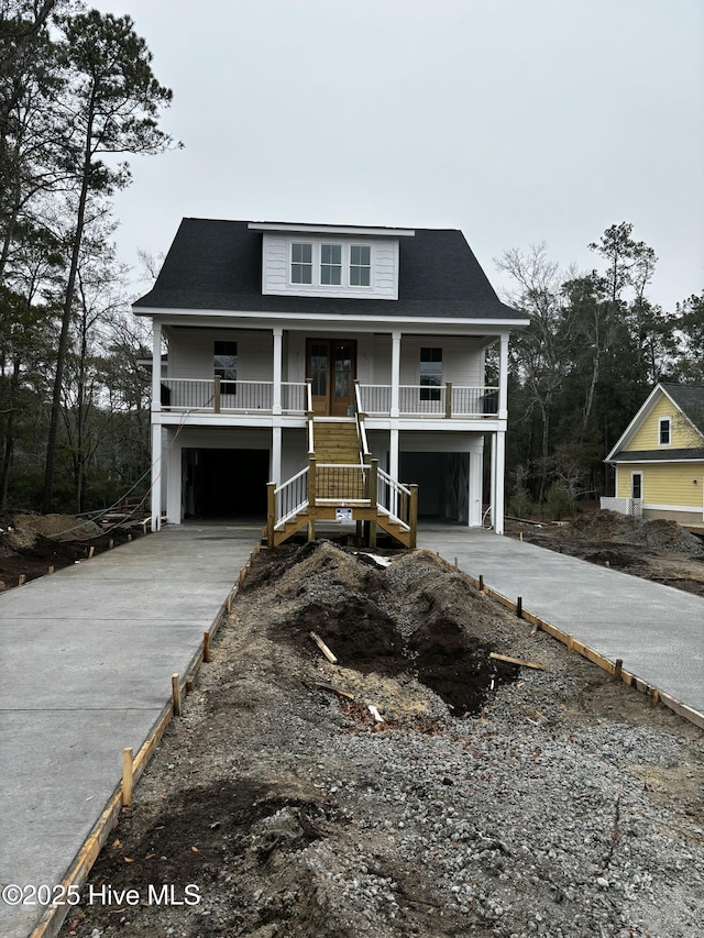 raised beach house with covered porch, concrete driveway, french doors, and an attached garage