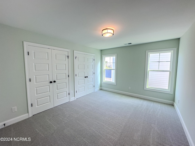 unfurnished bedroom featuring light colored carpet and two closets