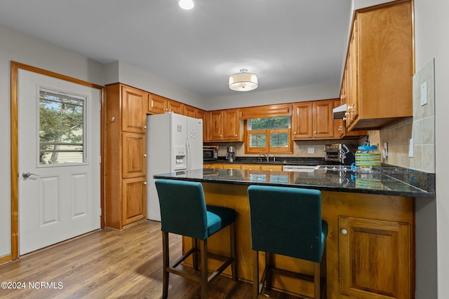 kitchen with hardwood / wood-style flooring, white fridge with ice dispenser, tasteful backsplash, kitchen peninsula, and a breakfast bar area