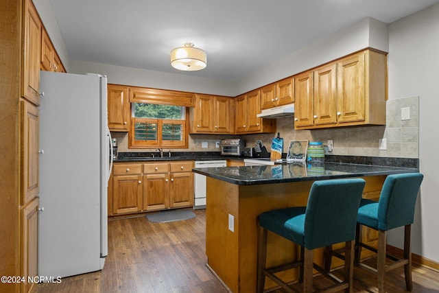 kitchen featuring dark hardwood / wood-style flooring, kitchen peninsula, white appliances, a breakfast bar area, and decorative backsplash