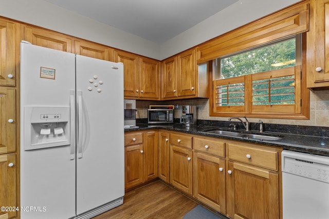 kitchen with hardwood / wood-style floors, white appliances, dark stone counters, sink, and decorative backsplash