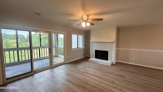 unfurnished living room with ceiling fan, a tiled fireplace, and dark hardwood / wood-style flooring