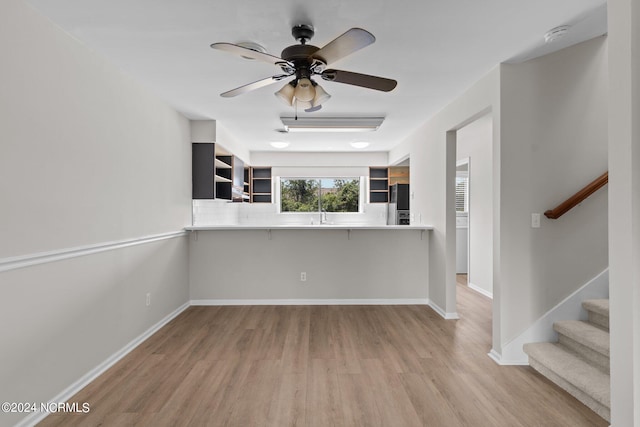 kitchen featuring light hardwood / wood-style floors, ceiling fan, a breakfast bar, black fridge, and kitchen peninsula