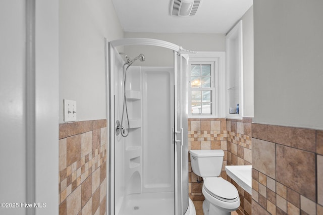 bathroom with a shower, tile walls, and toilet