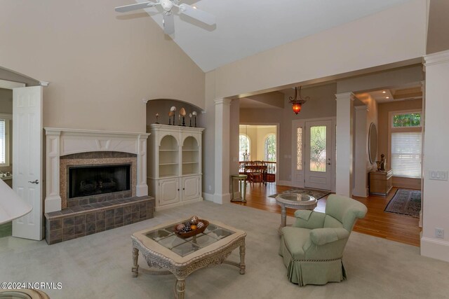 living room featuring ceiling fan, light hardwood / wood-style floors, ornate columns, a tile fireplace, and high vaulted ceiling