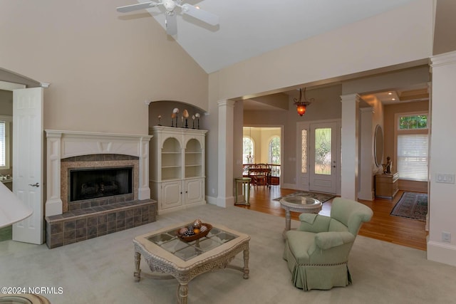 living room featuring high vaulted ceiling, a tiled fireplace, decorative columns, and baseboards