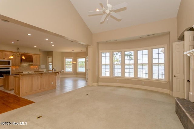 unfurnished living room featuring ceiling fan with notable chandelier, high vaulted ceiling, recessed lighting, light carpet, and baseboards