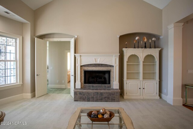 unfurnished living room with decorative columns, a tiled fireplace, high vaulted ceiling, and light colored carpet