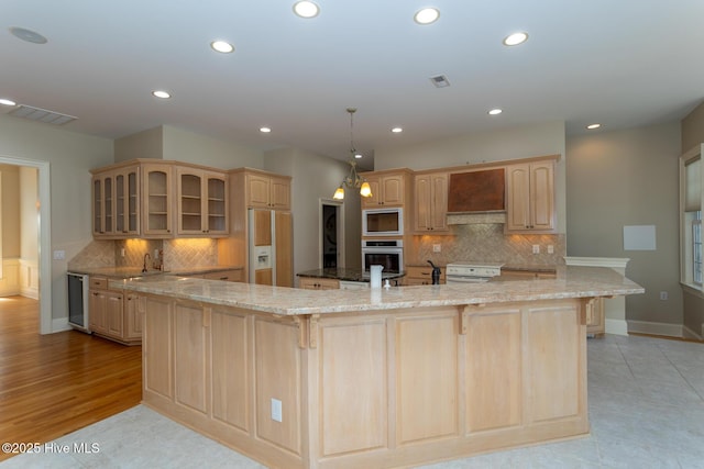 kitchen featuring custom range hood, built in appliances, a large island, glass insert cabinets, and visible vents