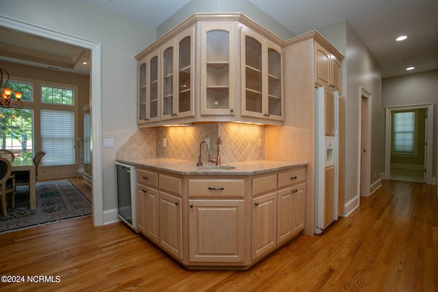 kitchen with light wood-type flooring, light stone countertops, light brown cabinetry, white refrigerator with ice dispenser, and decorative backsplash