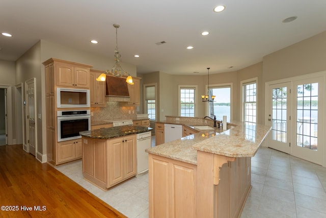 kitchen with custom range hood, white dishwasher, oven, built in microwave, and a spacious island