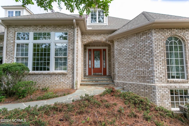 doorway to property featuring a shingled roof and brick siding