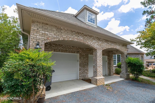 exterior space with an attached garage, brick siding, gravel driveway, and a shingled roof