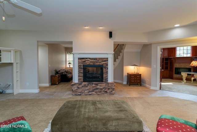 carpeted living room featuring a stone fireplace and ceiling fan