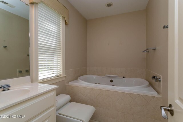 bathroom featuring vanity, toilet, and tiled bath