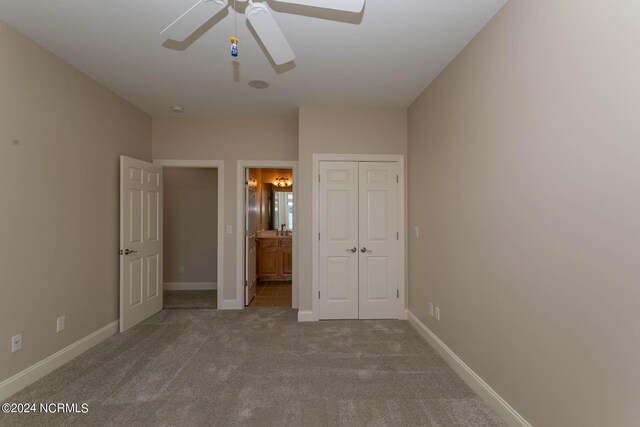 unfurnished bedroom with a closet, ensuite bathroom, ceiling fan, and carpet floors