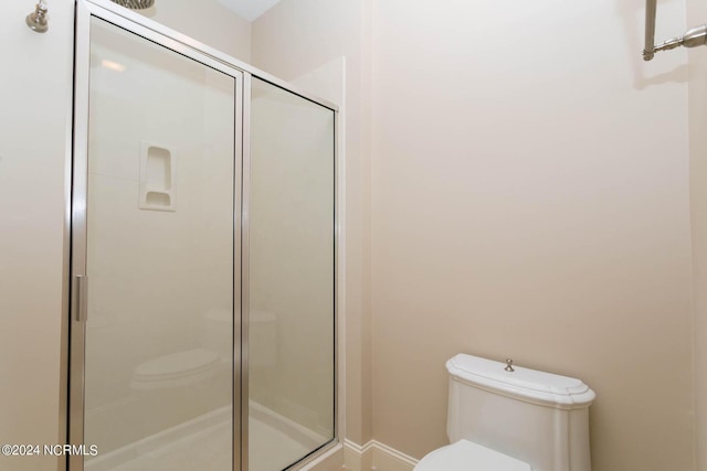 bathroom with toilet, a stall shower, and baseboards