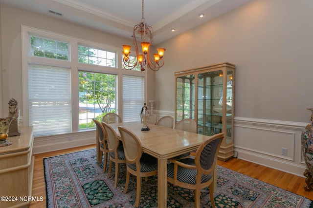 dining room with a wainscoted wall, wood finished floors, visible vents, ornamental molding, and an inviting chandelier