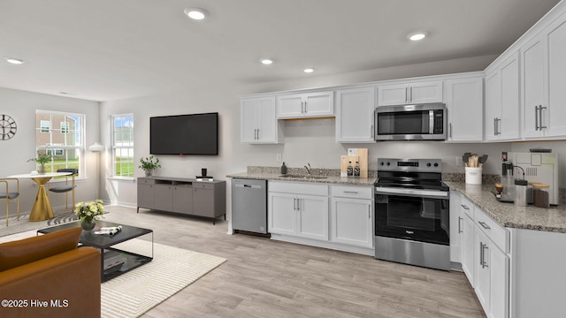 kitchen featuring light stone countertops, stainless steel appliances, sink, light hardwood / wood-style flooring, and white cabinets