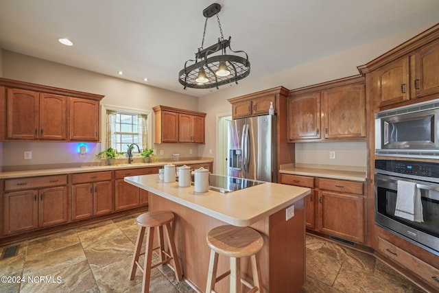 kitchen featuring sink, hanging light fixtures, appliances with stainless steel finishes, a kitchen breakfast bar, and a kitchen island