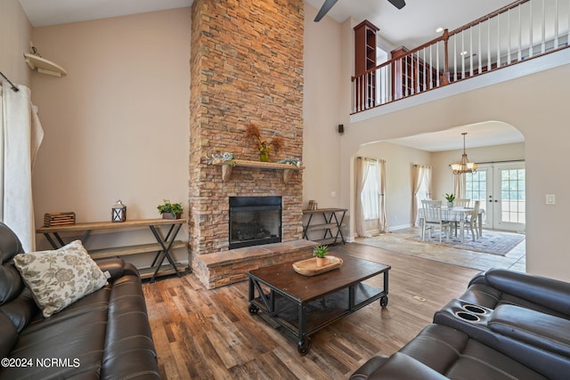 living room with ceiling fan with notable chandelier, a towering ceiling, a fireplace, and hardwood / wood-style floors