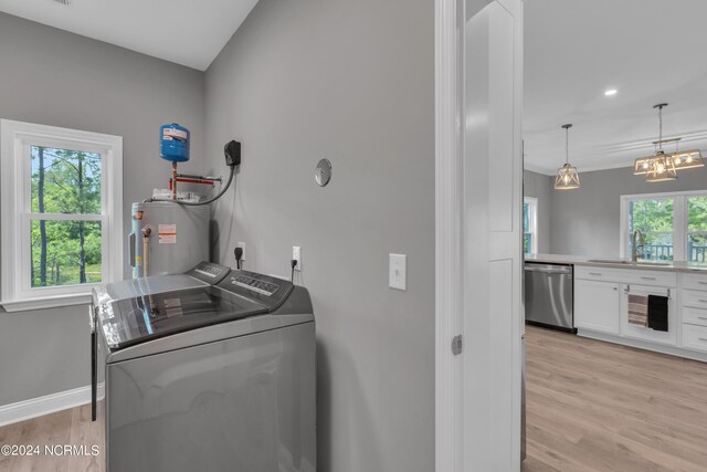 clothes washing area with sink, water heater, washer and dryer, a chandelier, and light wood-type flooring