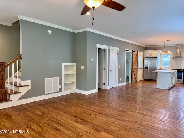 unfurnished living room with wood-type flooring, ceiling fan with notable chandelier, crown molding, and a barn door