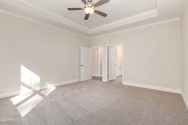 unfurnished bedroom with ensuite bath, light colored carpet, ornamental molding, a tray ceiling, and ceiling fan