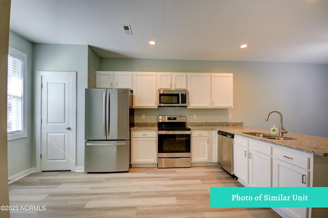 kitchen featuring kitchen peninsula, light stone counters, stainless steel appliances, sink, and white cabinetry