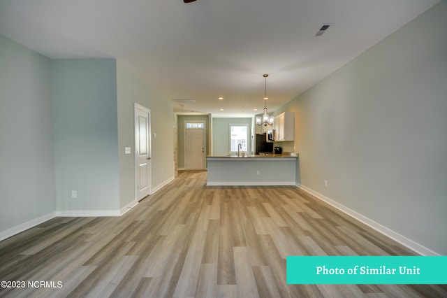 unfurnished living room with an inviting chandelier, sink, and light wood-type flooring