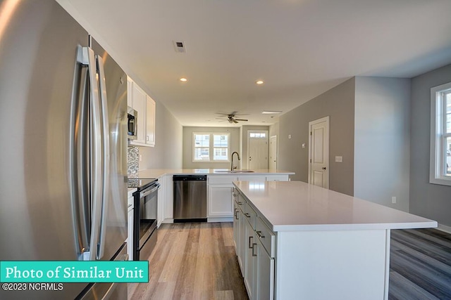 kitchen featuring sink, stainless steel appliances, a kitchen island, kitchen peninsula, and white cabinets