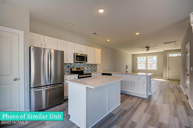 kitchen with kitchen peninsula, appliances with stainless steel finishes, sink, white cabinets, and a center island