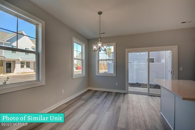 unfurnished dining area with wood-type flooring and a notable chandelier