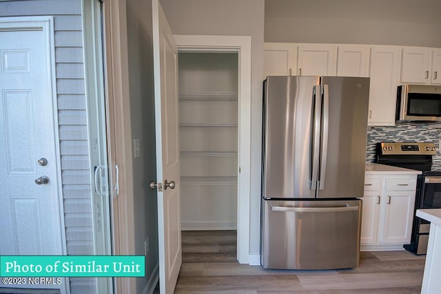 kitchen with white cabinets, decorative backsplash, light hardwood / wood-style floors, and stainless steel appliances